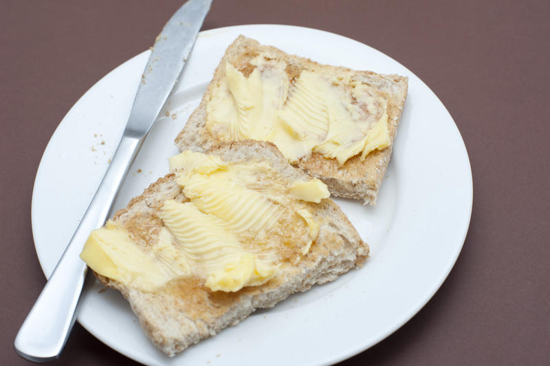 Close up Tasty Toasted Bread with Butter on Top Served on White Round Plate with Knife. Isolated on Brown Background.