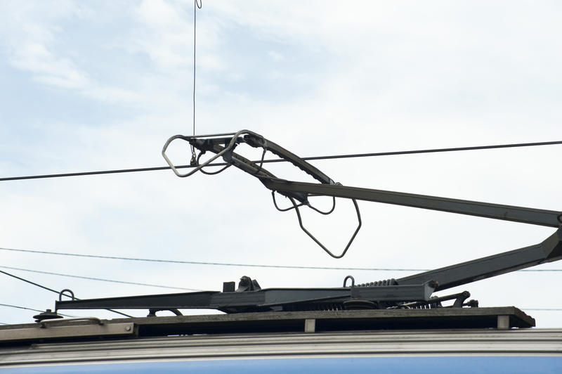 Pantograph on top of a train connected to overhead power lines, close up detail