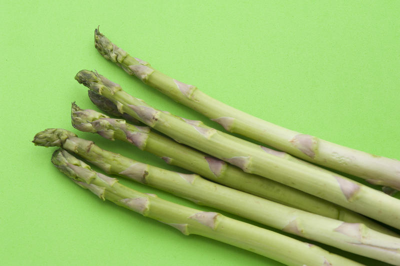 Overhead close up view of five fresh green asparagus spears or shoots on a light green background with copyspace