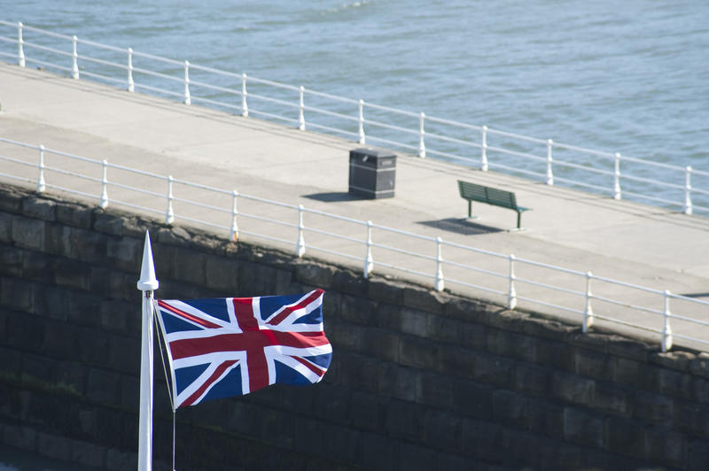 Union flag of the United Kingdom flying from a flagpole above the stone piers at the entrance to Whitby harbour