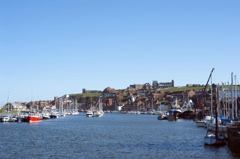 View across the upper fishing harbour with its moored fishing vessels at Whitby towards the abbey ruins outlined against a blue sky on top of the hill