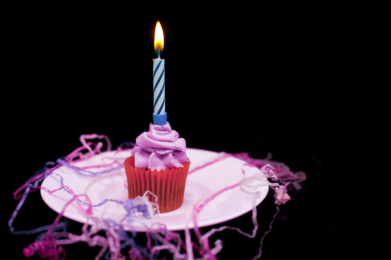 a small cup cake with pink icind, a candle and paink and blue celebration streamers