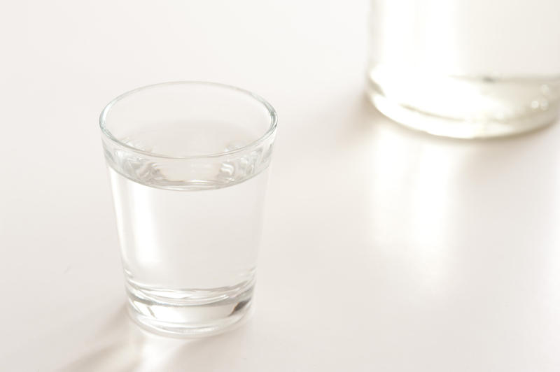 Shot glass full of clear vodka on a white background with the base of the bottle behind, with copyspace