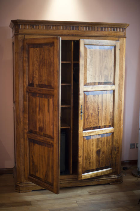Rustic wooden wardrobe or armoire in a bedroom with its double doors atnding ajar to reveal the empty storage shelves inside