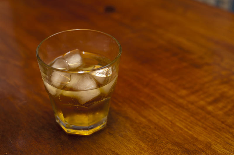 Close up Small Glass of Cold Whiskey with Ice on Top of Wooden Table