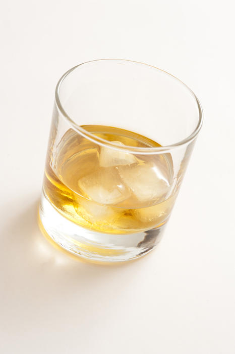 Whiskey on the rocks with ice cubes in a plain glass tumbler, high angle view on white