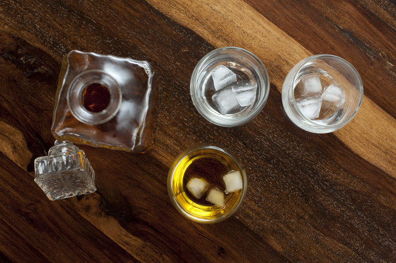 High Angle View of Whisky in Glass Decanter on Wooden Table with Copy Space Beside Three Glass Tumblers Containing Ice Cubes