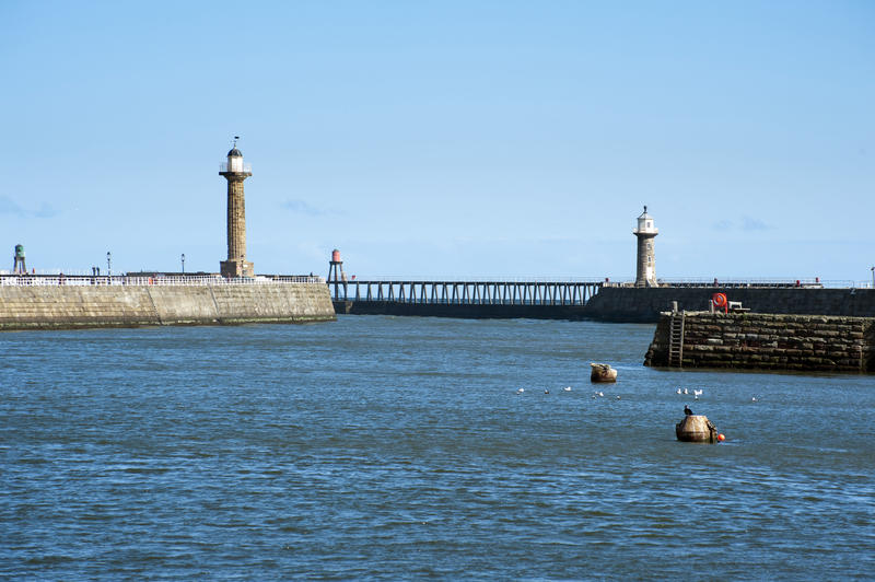 View across the water of the harbour to the Whitby stone piers and breakwaters with their navigation lighthouses on the Yorkshire coast