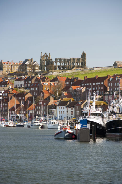 View of small fishing boats moored in the Whitby upper harbour with the ruins of Whitby Abbey visible on the skyline behind