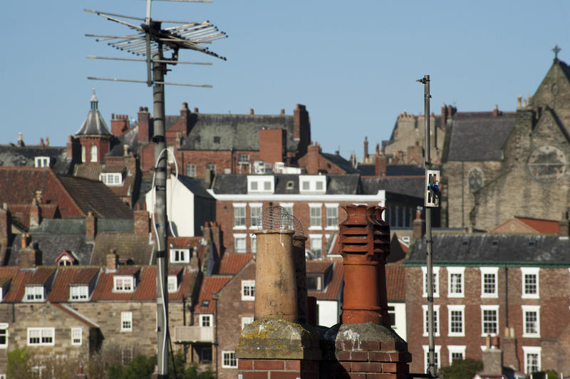 Whitby roofscape with clay chimney pots and a television aerial against a backdrop of traditional historic English houses