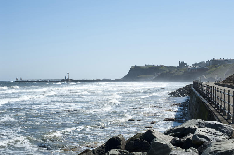 View from Whitby North Promenade looking across the surf and waves to the town of Whitby and its breakwaters at the entrance to the harbour
