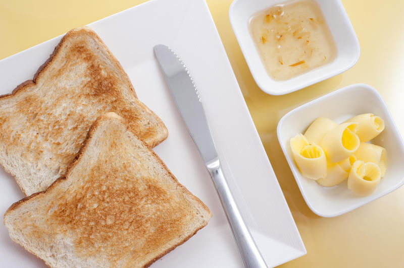Overhead view of two slices of white toast served with butter coils and marmalade on the side for breakfast