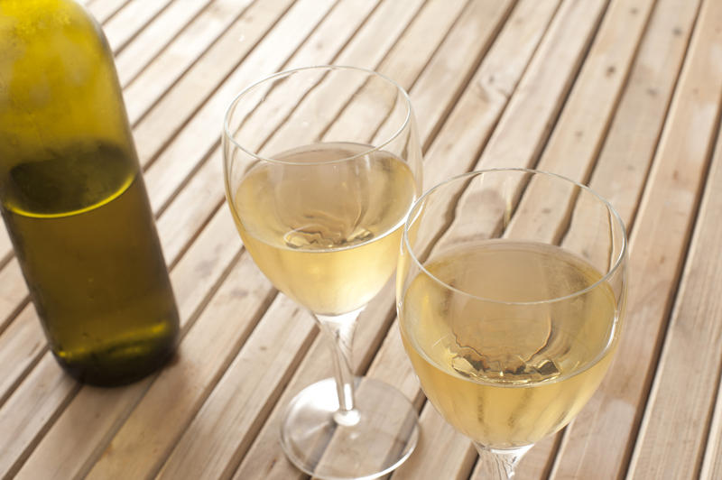 Two poured glasses of white wine with a half full unlabelled bottle alongside on a wooden slatted table with copyspace