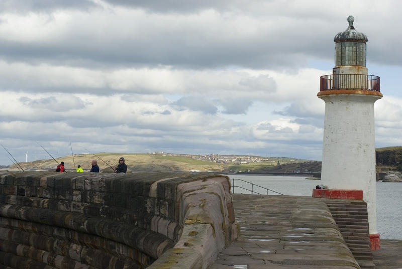 Whitehaven harbour seawall with the small lighthouse beacon and fisherman enjoying a days recreational fishing