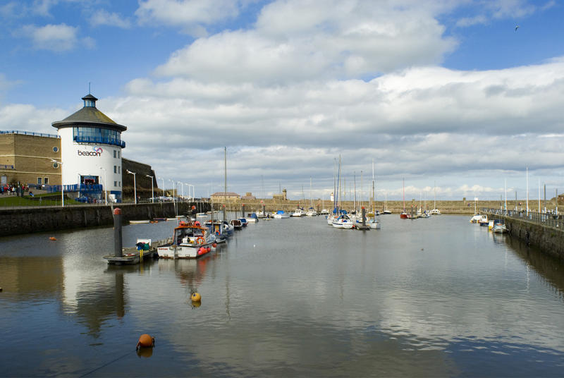 View of an inner basin at Whitehaven harbour with moored fishing boats and the beacon used to guide ships into harbour