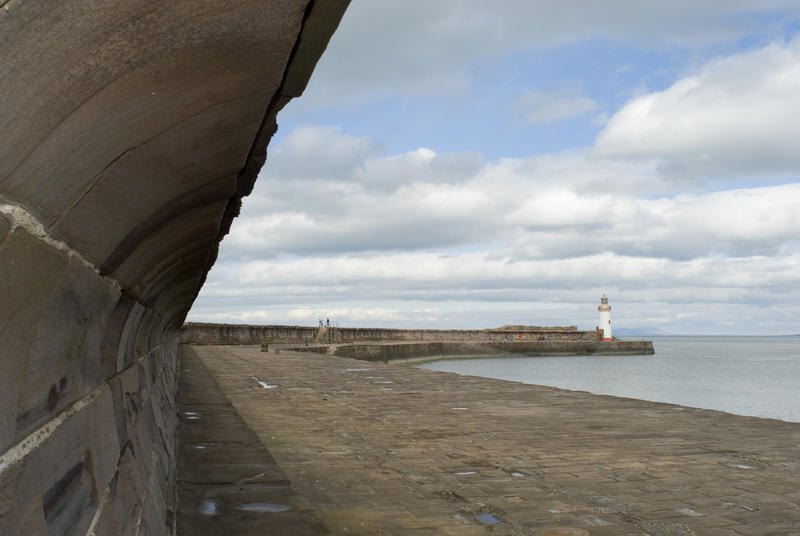 View along a deserted Whitehaven harbour seawall with the two beacons guarding the entrance to the breakwater visible in the distance on a calm day
