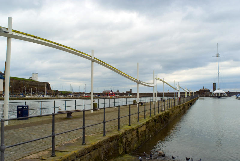 View along a deserted seawall and promenade at Whitehaven harbour with moored pleasure yachts visible in the distance