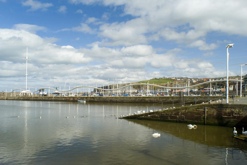 View over tranquil water to the slipway in Whitehaven harbour in Cumbria with the quay and waterfront visible behind
