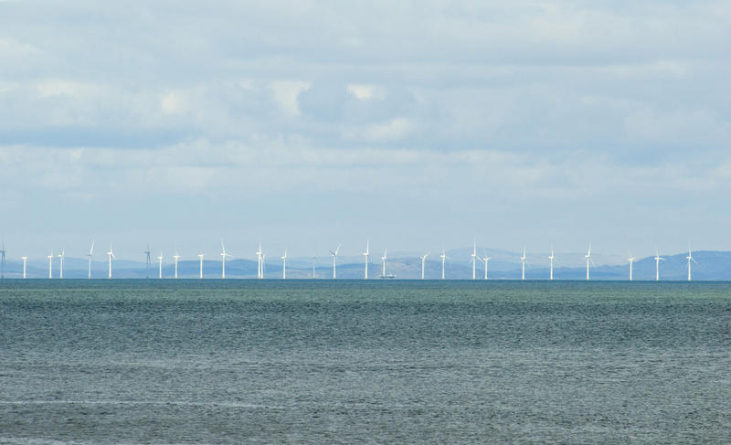 View across a calm ocean of a row of wind turbines in an offshore windfarm generating power and electricity from the kinetic energy of the wind