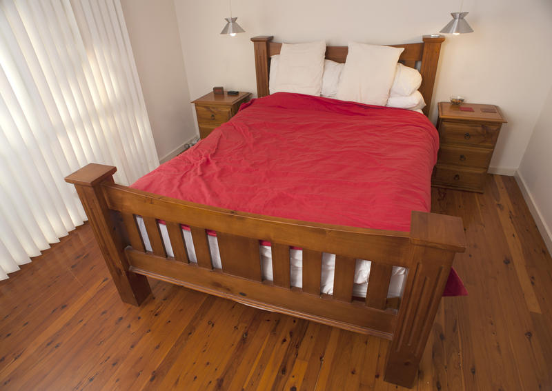 Wood frame double bed with headboard and footboard in a classic bedroom with a hardwood floor and floor length window
