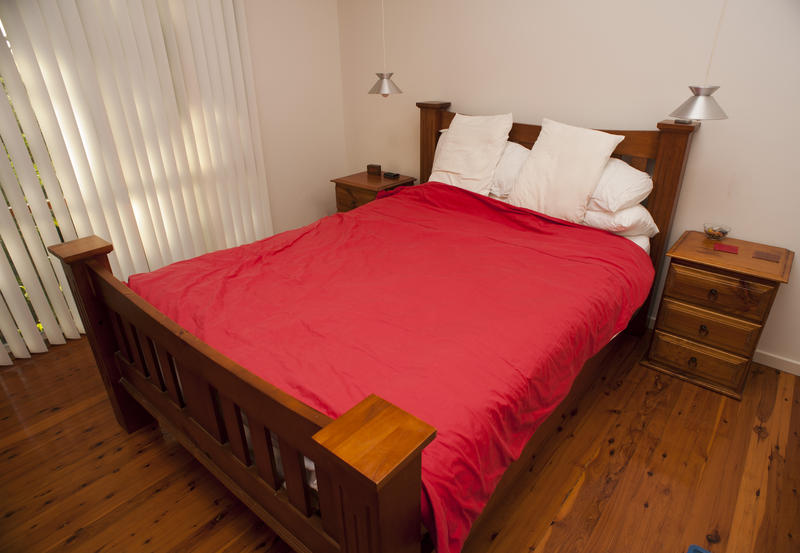 Old-fashioned wooden bed with a colorful red cover and fresh white pillows in a small bedroom with a hardwood floor