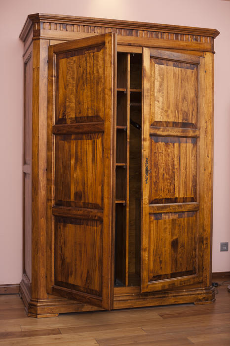 Large old rustic wooden wardrobe or cabinet used to store clothing standing in a bedroom with its doors slightly ajar to reveal the empty shelving inside