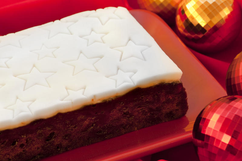Uncut commercial Christmas fruit cake with a decorative white icing impressed with a pattern of stars on a platter on a festive Christmas table