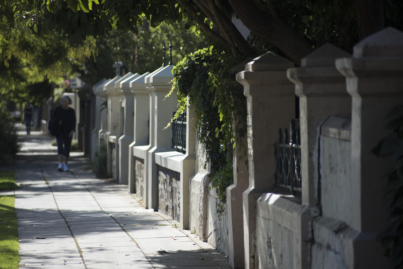 Historic house gates in a street in Adelaide, South Australia with a view down a shady leafy green sidewalk with a person walking in the distance