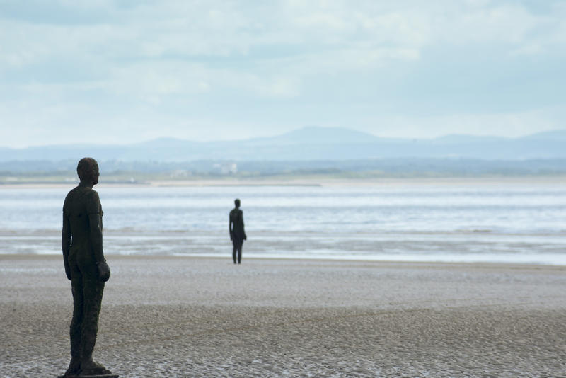 Two statues from the Antony Gormley artwork Another Place on the beach at Crosby UK standing facing towards the ocean, with copy space