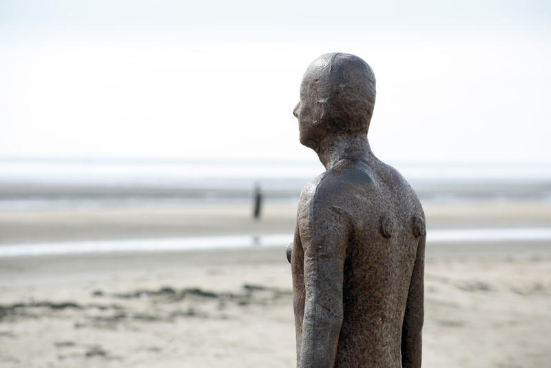 Close up a beach statue from Another Place by Antony Gormley, Crosby, UK facing out towards the ocean with copy space