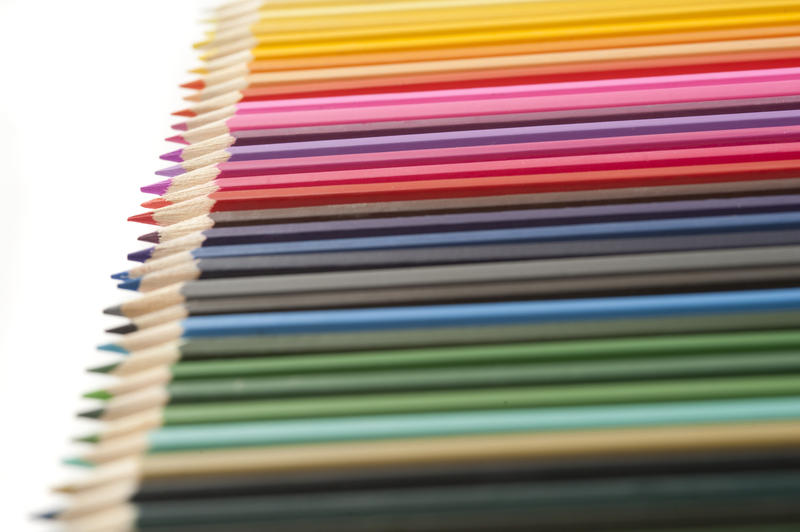 Array of newly sharpened pencils in dark and bright colors arranged in a long row with selective focus