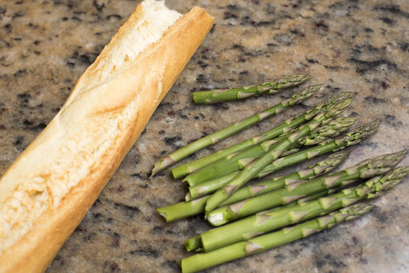French baguette on granite counter top in kitchen beside small bunch of asparagus