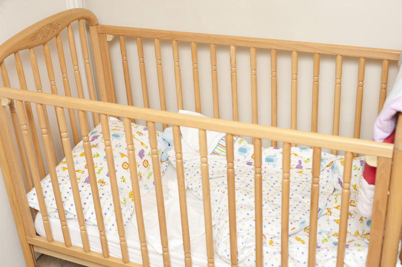 Empty pine colored wooden baby crib with folded over blanket in corner of room