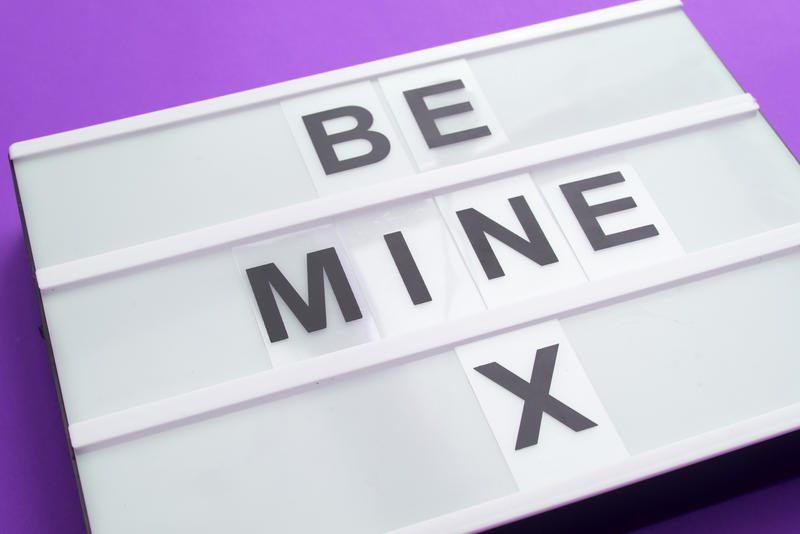 Close-up of white lightbox with BE MINE X message of black changeable letters over purple background