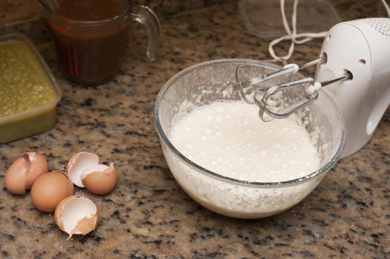 Whisking fresh raw eggs for baking in a glass mixing bowl on a granite counter using a handheld electric beater