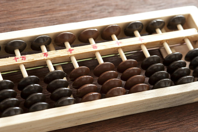 Close up on abacus with brown and black counters and hand written numbers on top of brown wooden table