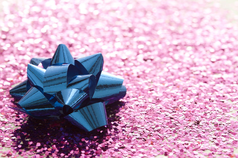 Shiny blue decorative ribbon bow on an oblique pink glitter background with copy space for a festive greeting