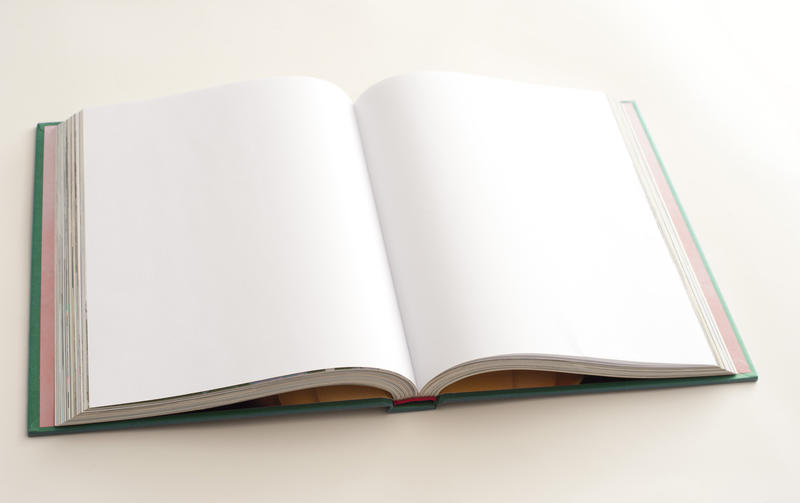 Open hardcover book with copy space over a double spread of blank white pages viewed at a low angle