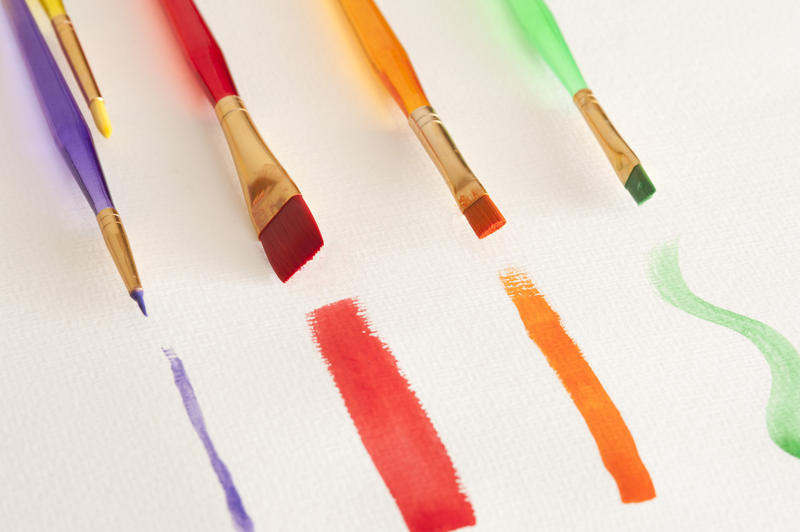 Thin, thick and medium plastic handle paintbrushes with purple, red, orange and green watercolor paintstrokes on white canvas paper