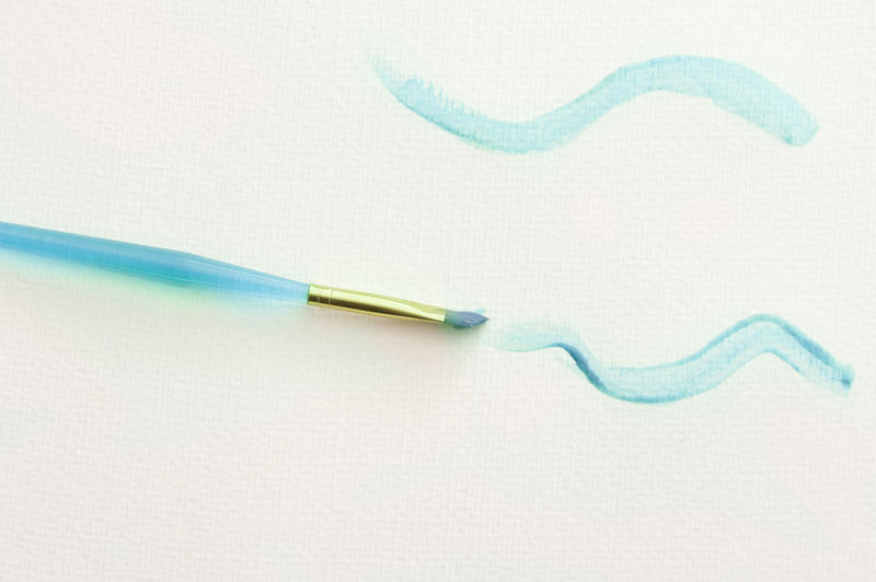 High Angle Still Life of Plastic Child Paintbrush Painting Squiggly Lines in Blue Paint on White Paper Background with Copy Space