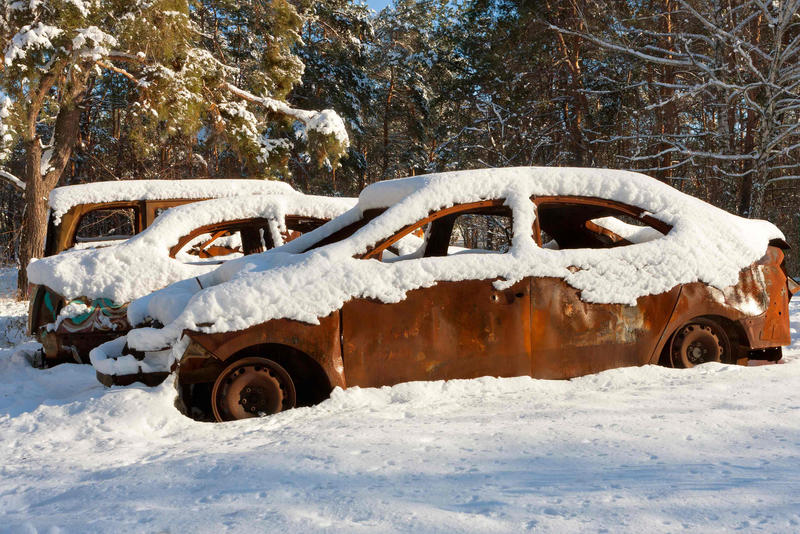 Burnt-out cars covered in snow on a sunny wintery morning against a forest background
