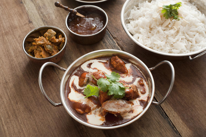 Assortment of delicious Indian cuisine of rice, meat and creamy sauce in metal serving pans on wooden table