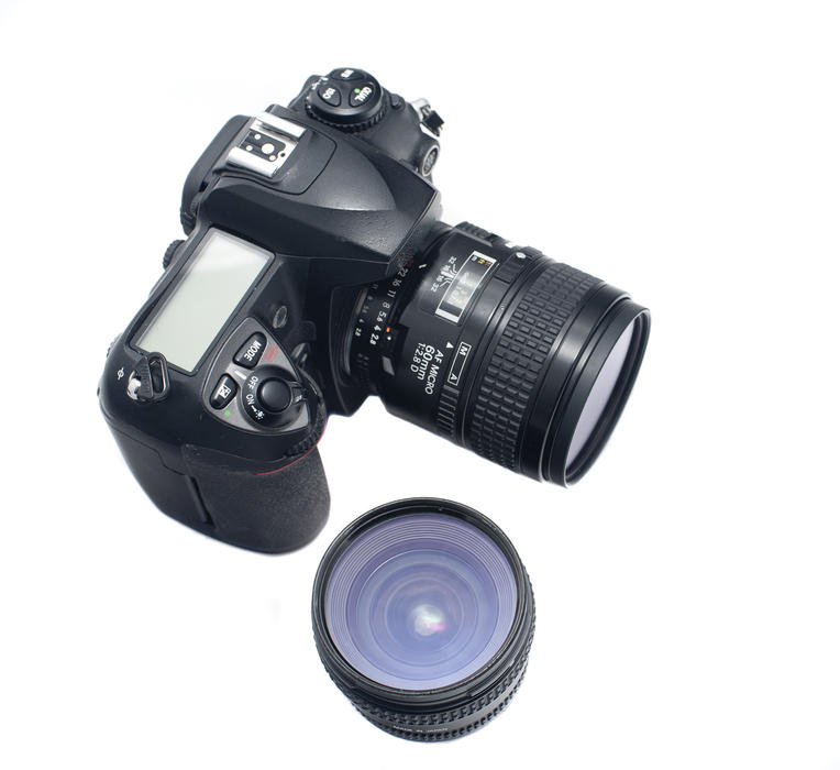 Single lens reflex camera with LCD display and detachable lenses over isolated white background