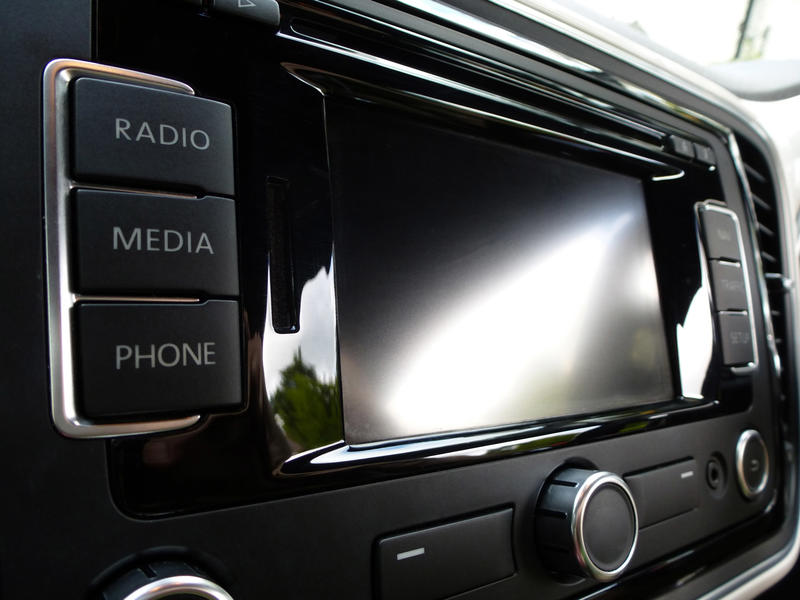 Blank digital car entertainment display on the dashboard viewed obliquely with the reflection of the sunlight on the surface and radio, media and phone buttons in the foreground