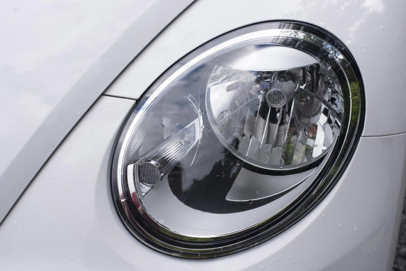 Car headlight unit in a sloping wing on a white car with recessed globe and lens