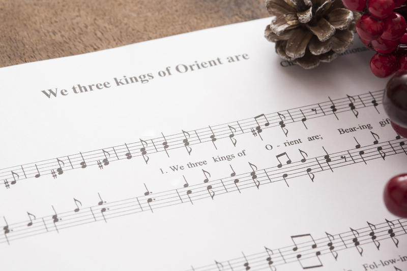 Christmas carol music with berries and pine cone decorations with a close up view of the score for We Three Kings Of Orient Are