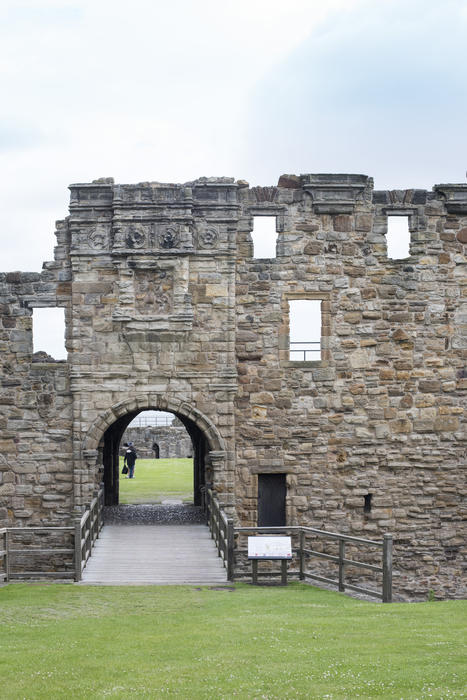 Ruined wall with a Gothic arch at St Andrews Castle, Scotland with people visible through the opening sightseeing on the grass beyond in a travel and tourism concept