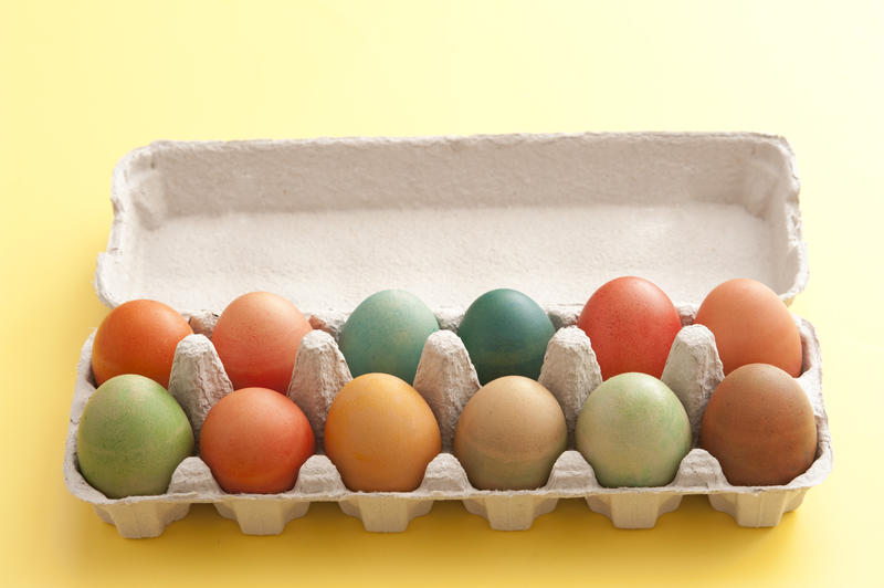 Cardboard carton of colorful dyed hard boiled fresh Easter eggs on a yellow background