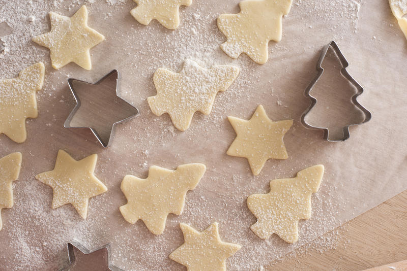 Making Christmas cookies with star and tree shaped cookie cutters in an overhead view of uncooked pastry shapes on oven paper