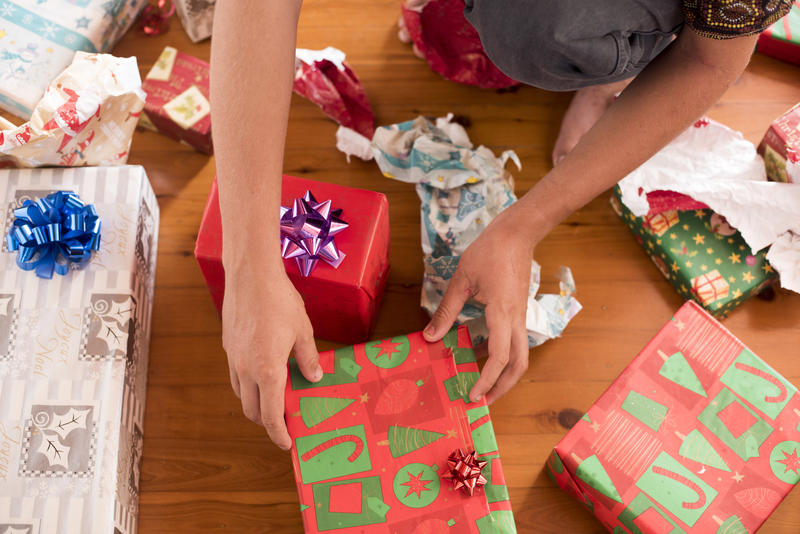 A close up of a teenager unwrapping Christmas presents on a timber floor.